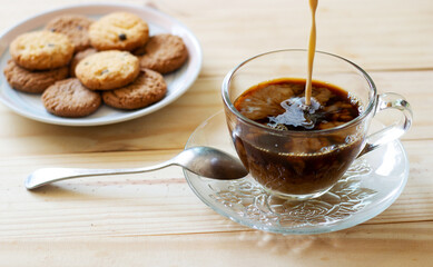 a cup hot coffee is mixing with milk.and cookies in plate .