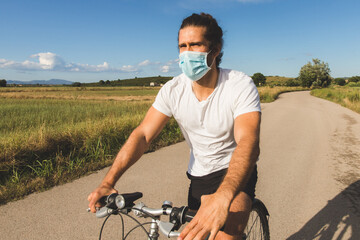 Young man on a bicycle on a country road wearing a mask