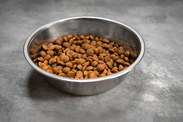 Dry dog food in a silver metal bowl on concrete floor.