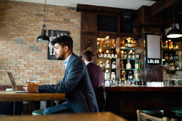 Portrait of a successful business man sitting at the cafe working on a laptop.