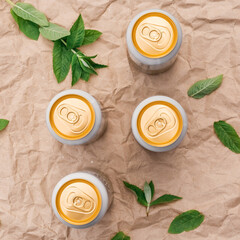 Four closed beer or soda gold aluminum cans, on a background of crumpled craft paper with mint leaves, top view, isolated, nobody. The concept of beer advertising.