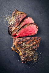 Barbecue dry aged angus rib of beef sliced with salt an pepper as top view  on a black board