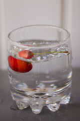 Ripe cherries in a glass with water on a table with a textured wooden wall