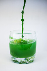 Green paint is poured into a transparent glass with clear water in the movement and paints clear water green on a white background.