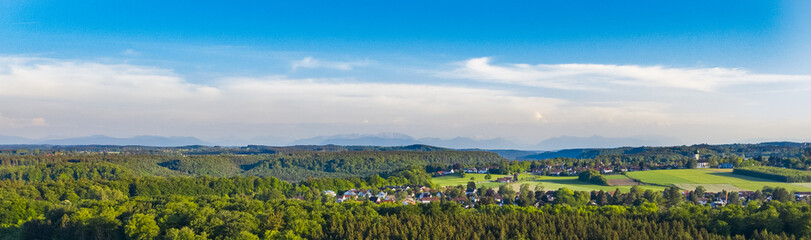 Fototapeta na wymiar Drone shot of German Bavaria typical town of Buchenhain bird view with Alps in the backround. Forstenrieder Park forest and fields next to town seen from above in spring