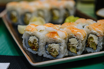Sushi pieces are placed on a ceramic plate. sprinkled with flying fish caviar. bowls with wasabi, cinder, ginger and soy sauce