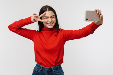 Photo of woman gesturing peace sign while taking selfie on cellphone