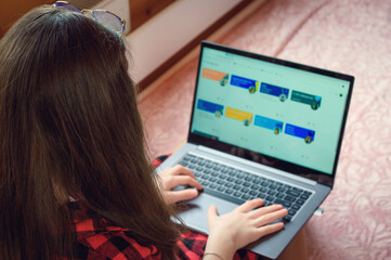 .Young schoolgirl learns lessons at a distance at home in a cozy wooden interior on the bed.