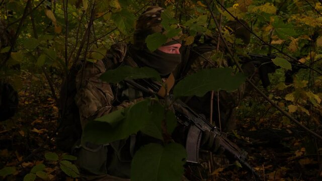 Masked commandos in the forest. A soldier with a rifle is watching closely. Special forces are hiding in an ambush, ready to attack.