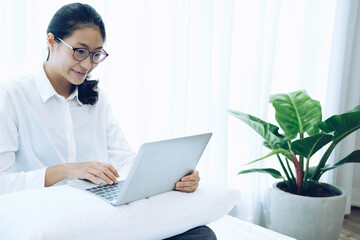 asian woman using computer on bed in bedroom. work remotely at home. leisure lifestyle