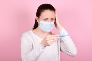 Portrait of a brunette girl in a medical mask looks at the thermometer.