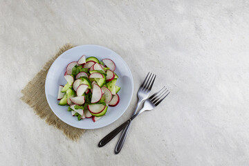 Spring salad of fresh radishes and cucumbers on a gray background, top view