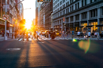 Bright light of sunset shines on the crowds of people crossing a busy intersection on 5th Avenue in...