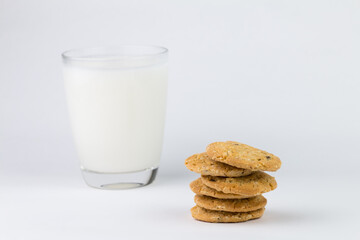 Closeup of the cereal cookies is stacked in multiple pieces and the cookies are brown and a cup of milk is placed behind them. The image has blank space beside the object and has a white background.