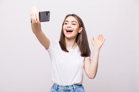 Portrait of a young attractive woman with greeting gesture making selfie photo on smartphone isolated on a white background