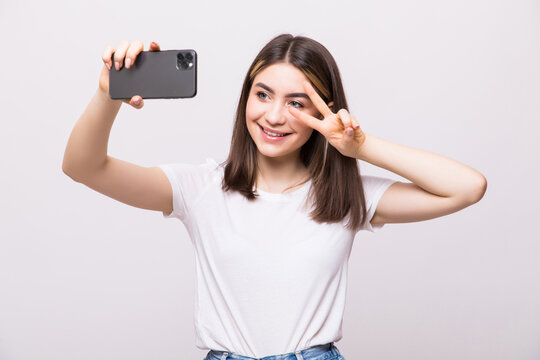 Portrait of a young attractive woman make peace sign making selfie photo on smartphone isolated on a white background
