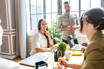 A midshot of young team discussing a start-up idea in contemporary office at the table, a view from the back of a young brunette. Multiracial team