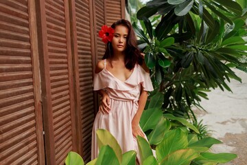 Playful Asian woman with hibiscus flower in hairs and in pink dress posing in luxury tropical resort. © Svetlana Sokolova