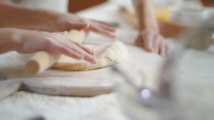 Mother teaching daughter to roll dough with rolling pin on kitchen table