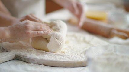 Mother hands helping daughter to knead dough on table at home