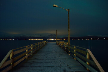 Obraz premium long snowy wooden pier with faint aurora borealis over mountain and fjord surface