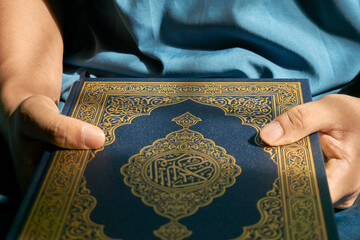 Close up of hand holding Holy Al Quran with written arabic calligraphy meaning of Al Quran