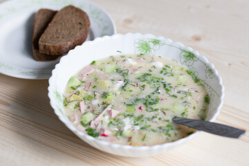 Cold soup okroshka with spoon and bread on wooden background