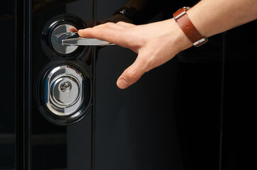 Glossy black metal entrance door with details: handle, open closed lock, hinges and threshold.