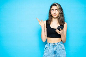 Portrait of a worried confused girl with mobile phone isolated over blue background