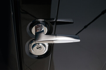 Glossy black metal entrance door with details: handle, open closed lock, hinges and threshold.