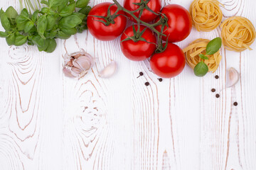 Top view raw tagliatelle pasta with fresh basil, garlic and tomatoes on a rustic white table, flat lay, copy space.