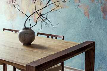 Close up of design wooden table with, stylish chairs, flowers in vase and elegant accessoreis. Details of home decor. Indusrtial concept of dining room. Open space. Template. Old wall.