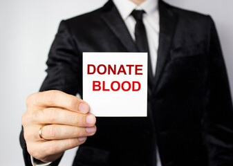 The word blood donation medical concept written in red letters on a white piece of paper in the hands of a businessman.