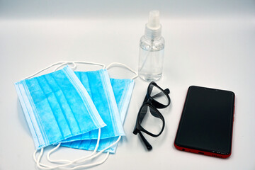 Surgical face mask, hand sanitizer, mobile phone and glasses over white background
