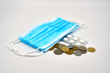 Surgical face mask, coins and medicine pills over white background