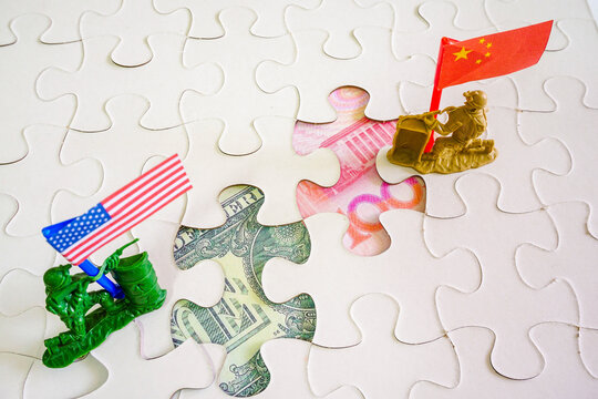 Conceptual image of unsettled USA-China trade war. 2 flag-bearing toy soldiers guarding respective currencies images in the missing jigsaw puzzles. Focus on US dollar.