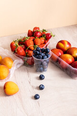 fruit composition with blueberries, strawberries, nectarines and peaches in plastic containers on wooden surface isolated on beige