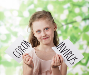 Girl on a background of green foliage holds a torn sheet with the inscription coronavirus. The...