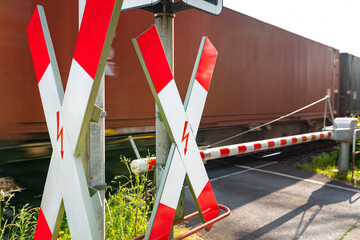 Closed barrier at the railway crossing with St. Andrew cross, visible blurred red wagon in motion.