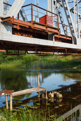 Fototapeta premium Metal constructions of the railway bridge over the river and the old pier. Reflections of constructions of a railway bridge on the surface of river water