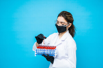 Woman doctor in a protective workwear is testing a blood sample tube in the medical laboratory isolated on blue background