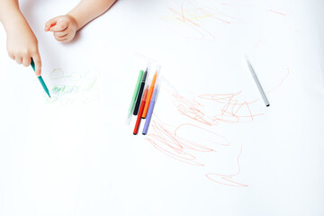 Little child draws on white paper with colored felt-tip pens, teaching children to draw
