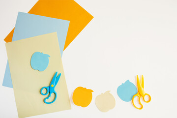 Several sheets of colored paper, two scissors, and Apple-shaped sticky notes on a white background. Flat layout with copyspace.