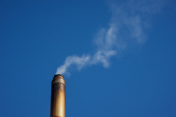 Metal smoke pipe with smoke on blue sky background. Copy space.