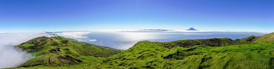 Panoramic view of green landscape above the clouds with Pico mountain in the distance, grass and...