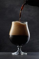 Stream pouring dark beer from the bottle into a beer glass.     Jet of the dark porter pours and...