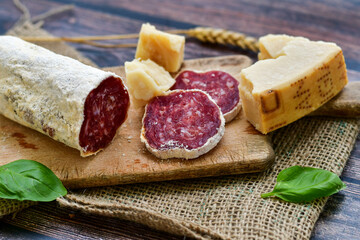Italian  dried   artisan  pork salami,parmesan cheese ,peperoncino  and fresh basil on wooden background .Rustic  home made food
