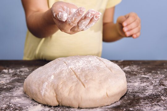 hands of a child putting flour on a bread dough