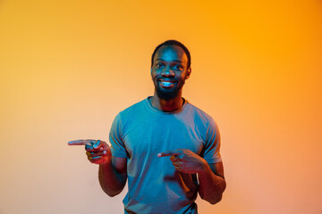 Pointing at side. African-american man's modern portrait on gradient orange studio background in...