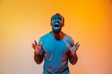 Angry screaming. African-american man's modern portrait on gradient orange studio background in neon light. Beautiful afro model. Concept of human emotions, facial expression, sales, ad. Copyspace.